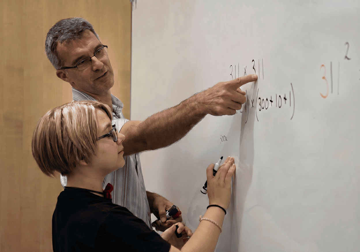 A Move Up Tutoring tutor pointing at math on a whiteboard while a student works through the problem